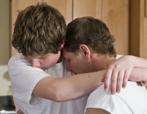 father and teenage son embrace, as if reconciling after conflict